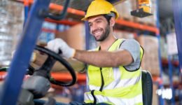Forklift Truck Operator Lifts Pallet Cardboard Boxes On a Shelf by Trucks smiling portrait