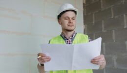 white male engineer or designer in helmet and safety vest at the construction site with a plan