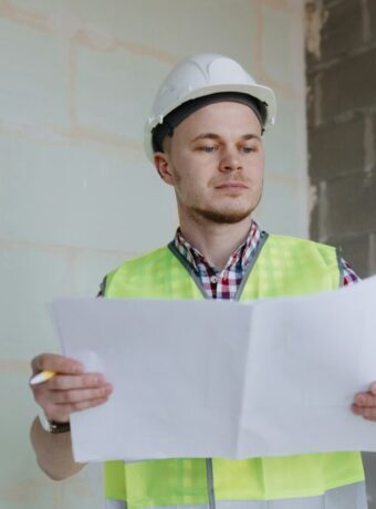 white male engineer or designer in helmet and safety vest at the construction site with a plan