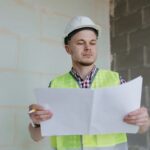 white male engineer or designer in helmet and safety vest at the construction site with a plan